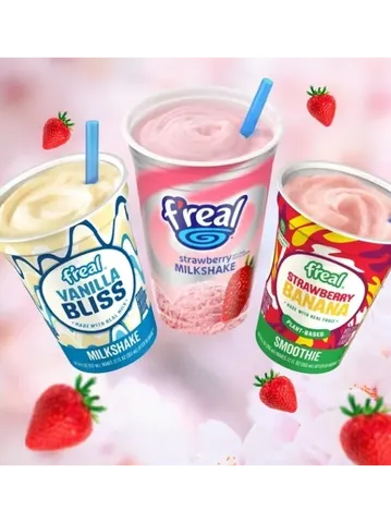 Three F'real drink cups: Vanilla Bliss milkshake, Strawberry milkshake, and Strawberry Banana smoothie, with strawberries and a light pink background.